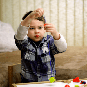 Little boy stringing beads on a string to practice fine motor skills.