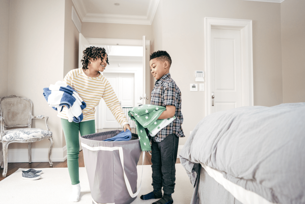 A smiling mother and her child folding laundry together, encouraging independence through daily chores.