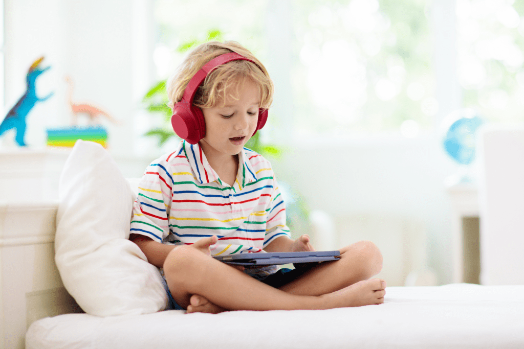 Young autistic child using a tablet with noise-canceling headphones, demonstrating sensory-friendly technology and communication tools.