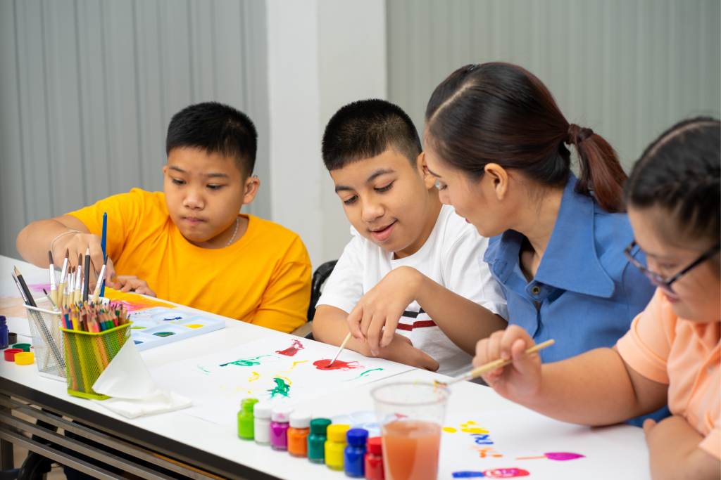 Children with autism engaging in a guided art activity with a caregiver, highlighting inclusive education and creativity through ABA therapy.