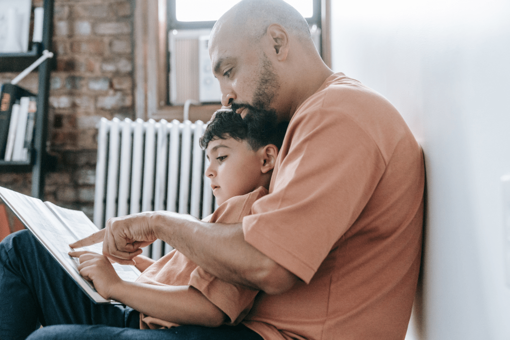 Father reading a book with his young autistic son, sharing a quiet and focused bonding moment at home