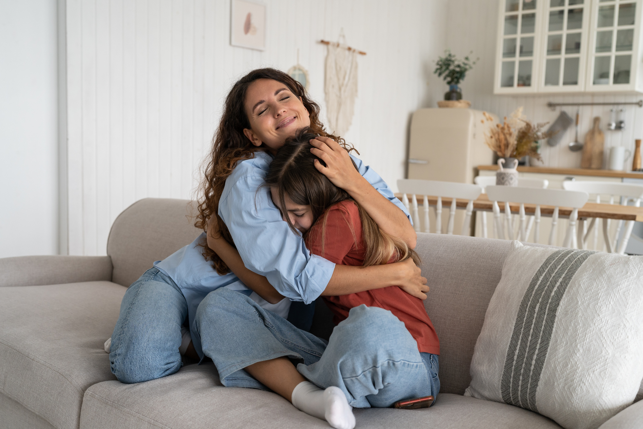 Alt text: Mother hugging autistic daughter on the couch, both smiling in a warm and supportive home environment