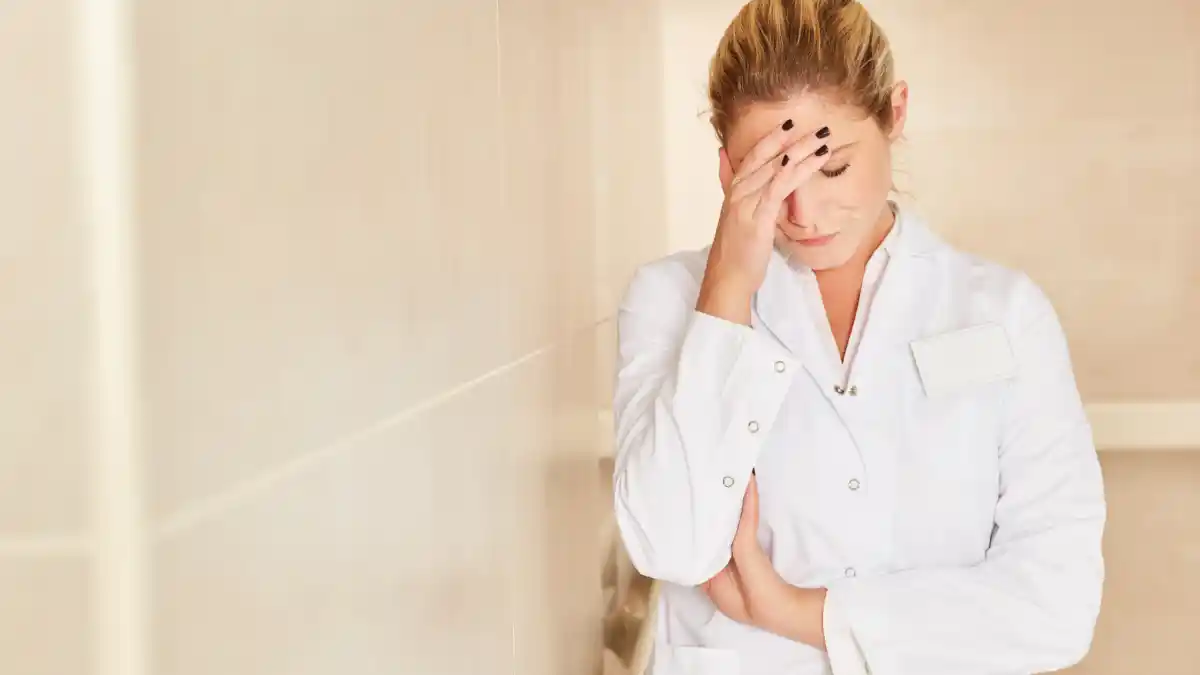 Worn out woman standing in a hallway with her head in her hands.