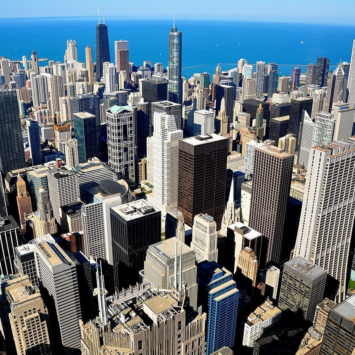 A dense city skyline with numerous skyscrapers along a blue harbor by the sea.